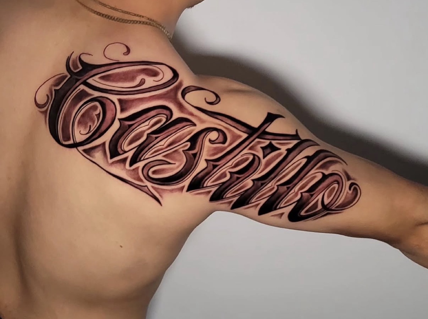 Custom script lettering tattoo with ornamental flourishes across the shoulder and upper arm